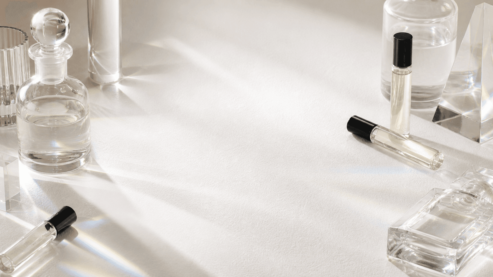 Glass fragrance decants and prisms on a warm paper-white studio surface.