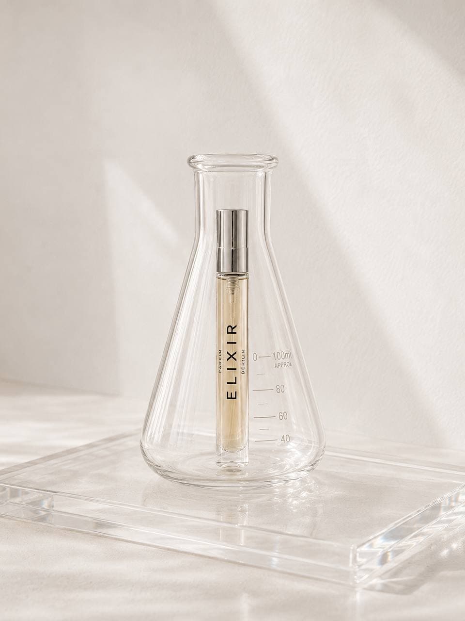ELIXIR fragrance vial displayed inside a clear laboratory flask on a luminous studio plinth.